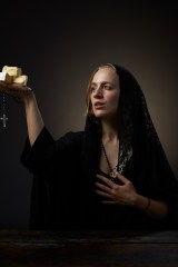 Photo of author Erika Kubick in a long black veil gazing in divine wonder at the sacred cheese cubes she holds in her hand. A rosary also dangles from the same hand.