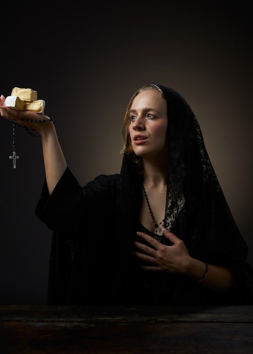 Photo of author Erika Kubick in a long black veil gazing in divine wonder at the sacred cheese cubes she holds in her hand. A rosary also dangles from the same hand.